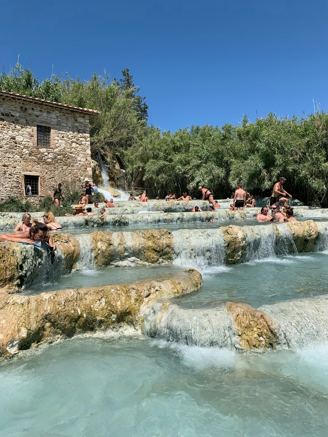 Persone si rilassano in sorgenti termali naturali circondate da architettura in pietra.